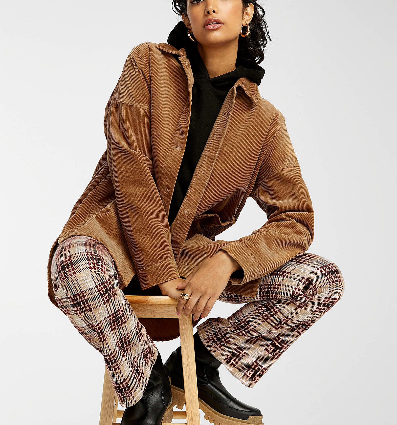 a person sitting on a stool wearing the corduroy jacket with checkered pants and rain boots
