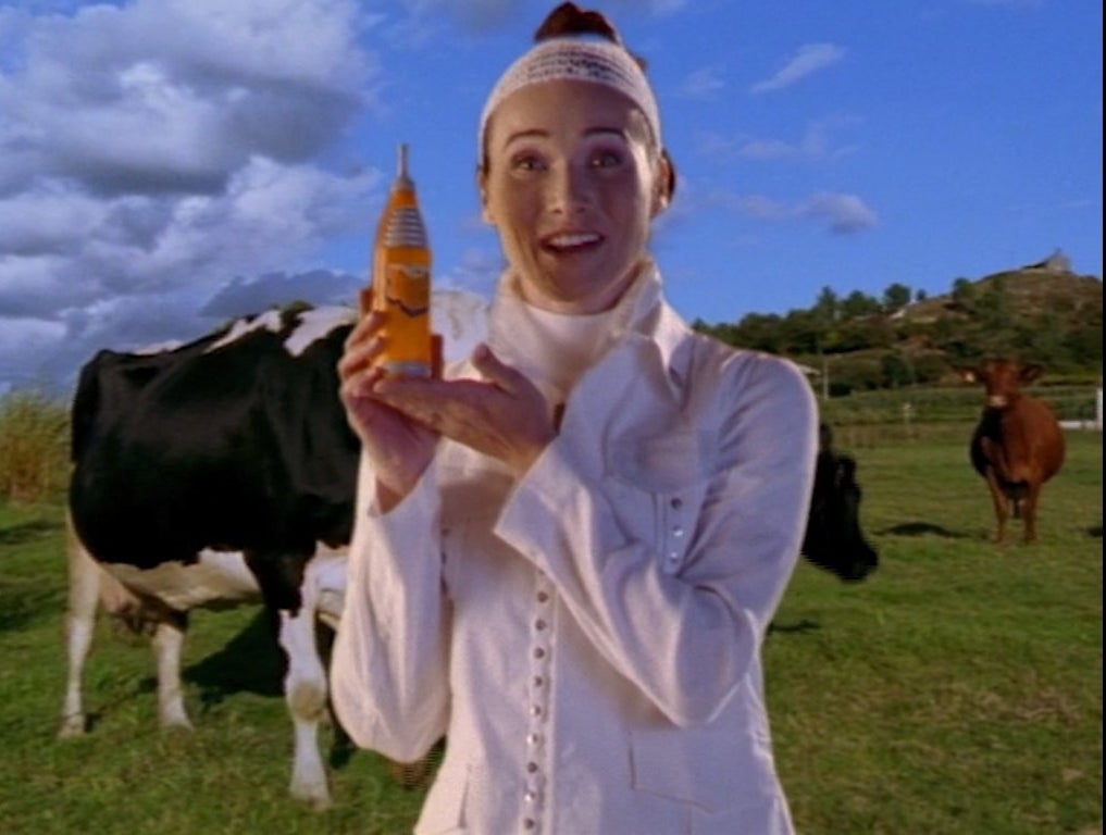 A woman holds a can of cheese soda in front of some cows