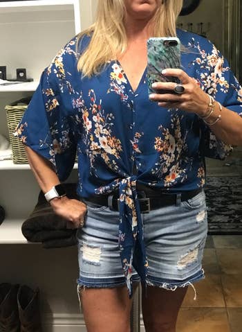 a reviewer wearing the shirt in blue with a multicolor floral print with denim shorts 