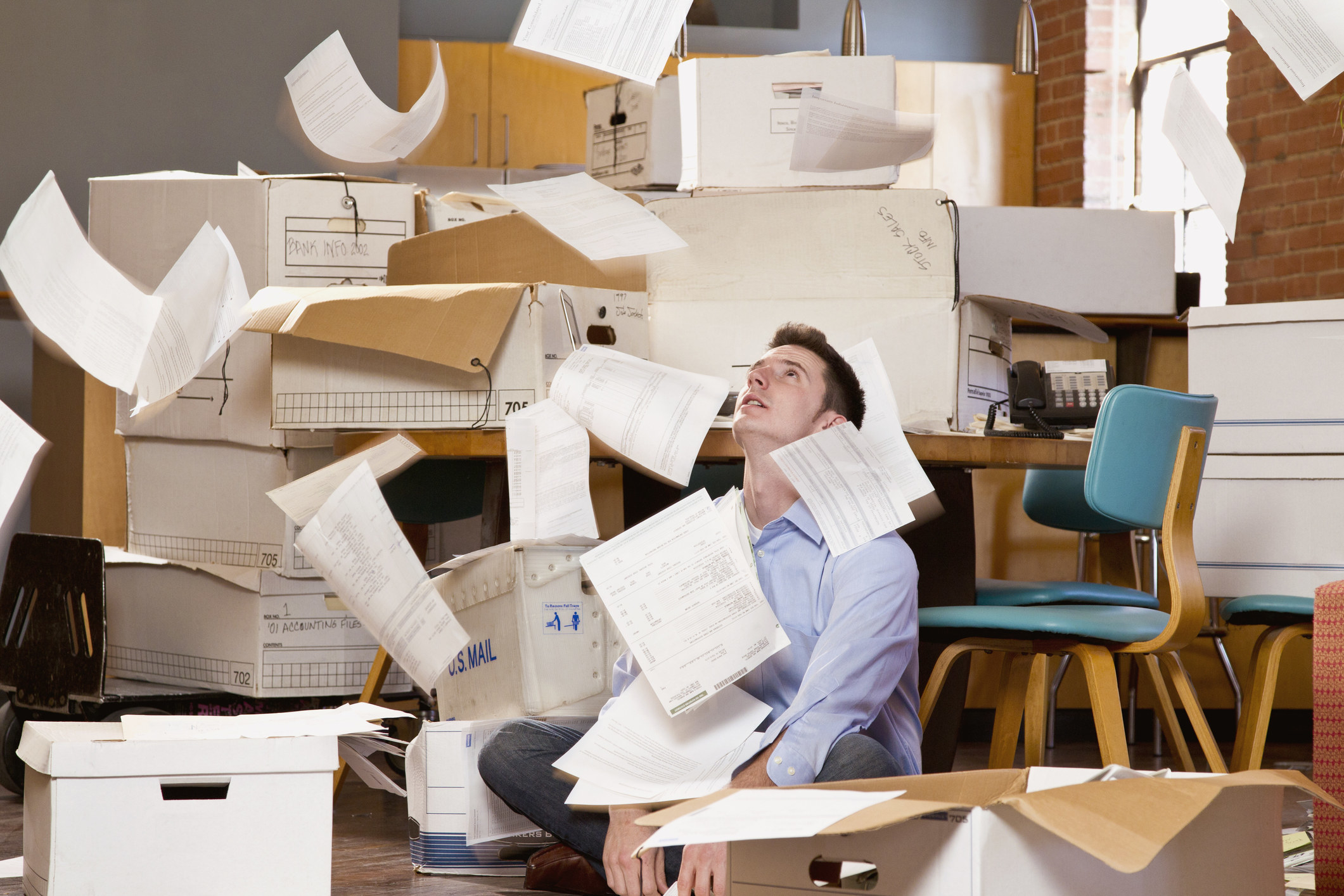 Person sitting in front of files and looking up at a bunch of papers thrown up in the air