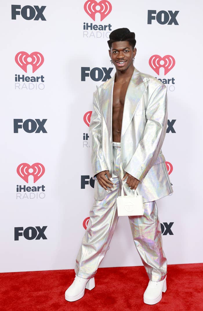 Lil' Nas X on the red carpet of an event in a metallic suit and platform heels