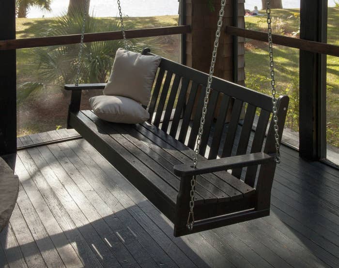 classic wooden porch swing in black hung up with standard chains