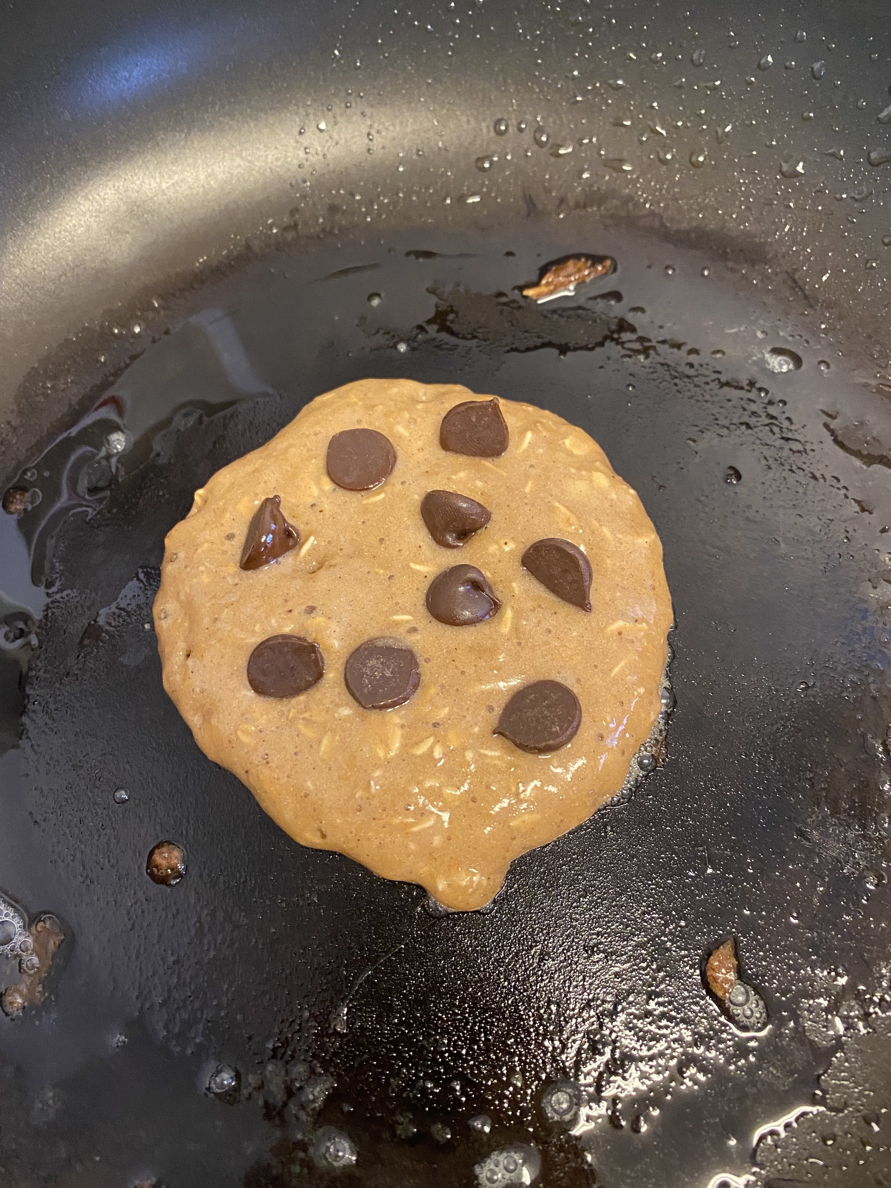 The pancake sizzling in the pan with chocolate chips added