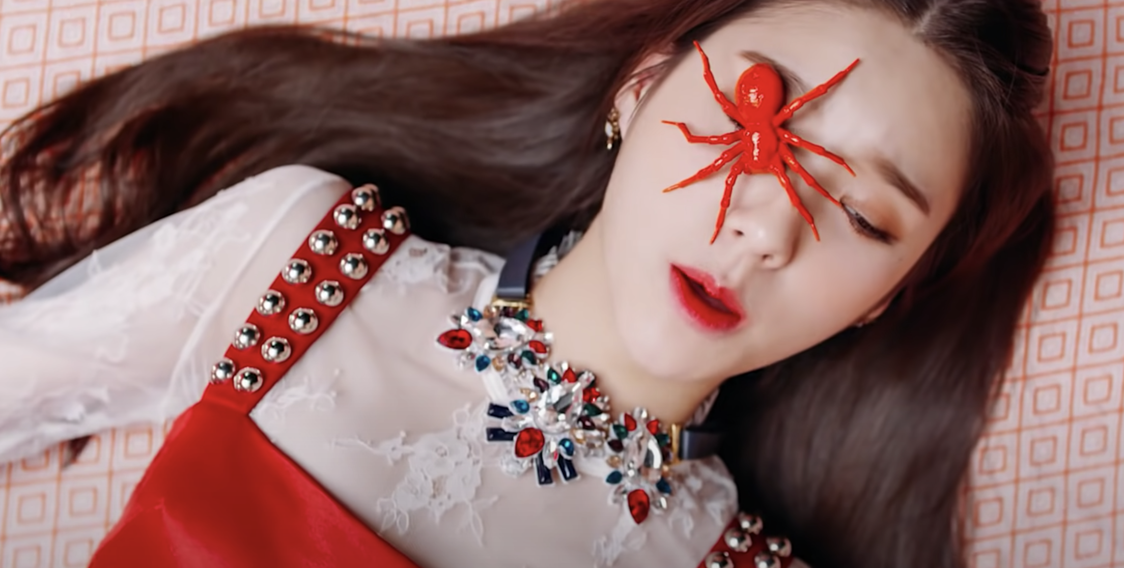 HeeJin lies on the floor with a fake spider covering one of her eyes
