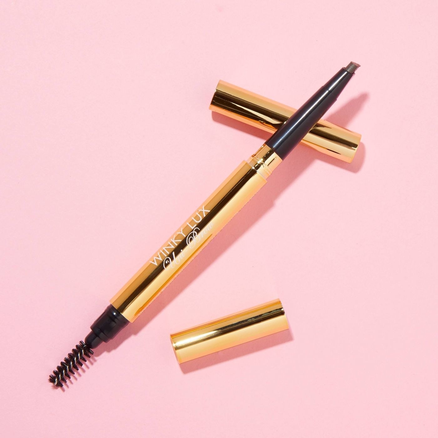 A dual sided brow pencil with an eyebrow brush on a pink backdrop