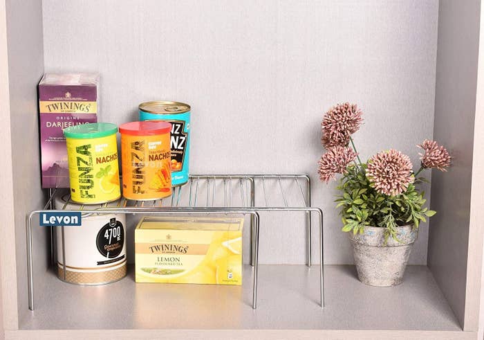 An expandable shelf with food items at the top and bottom and a flowerpot beside it