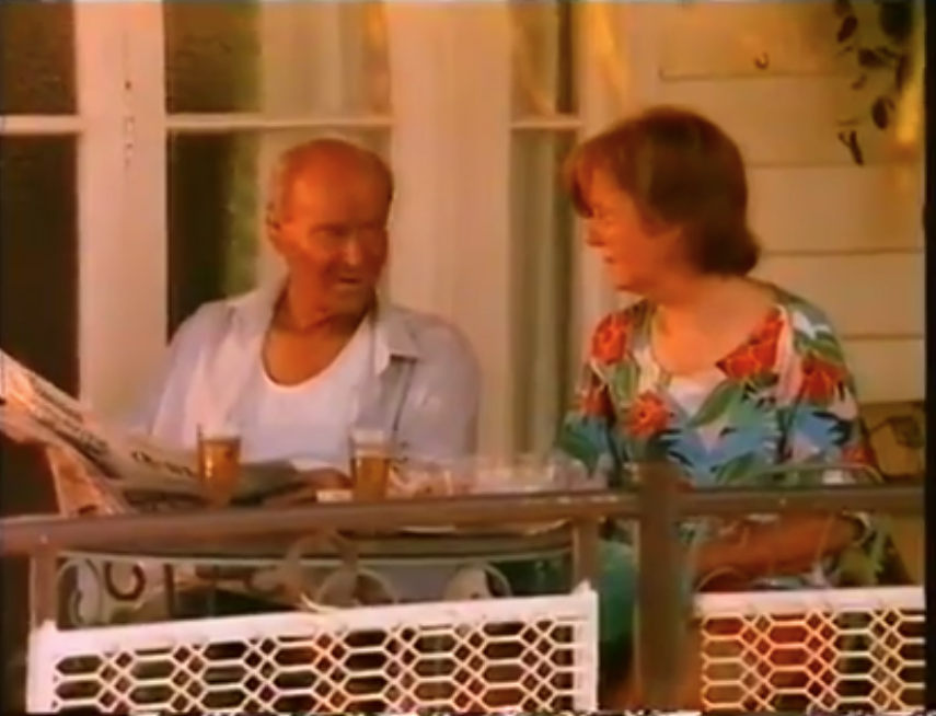 An older woman talks to her husband while sitting down on their balcony