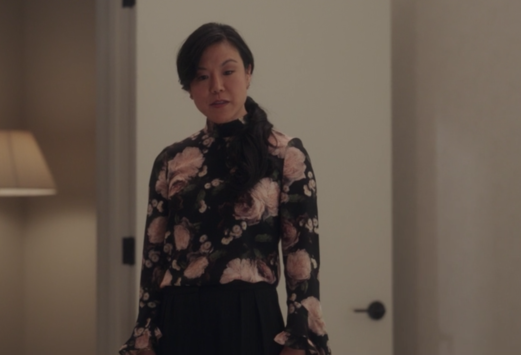 Jody wears a high-neck long sleeve floral blouse and dark dress pants
