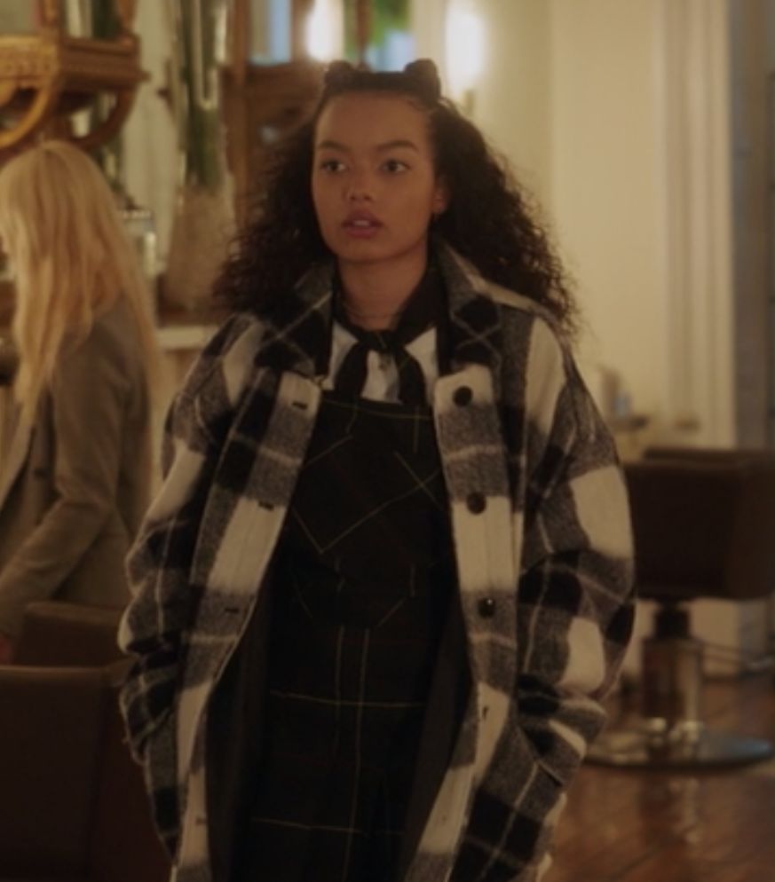 Zoya wears a plaid jumper skirt over a plain t-shirt under an oversized plaid coat