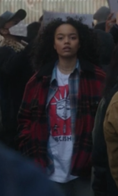 Zoya wears a baggy t-shirt under an open flannel shirt under a baggy flannel coat