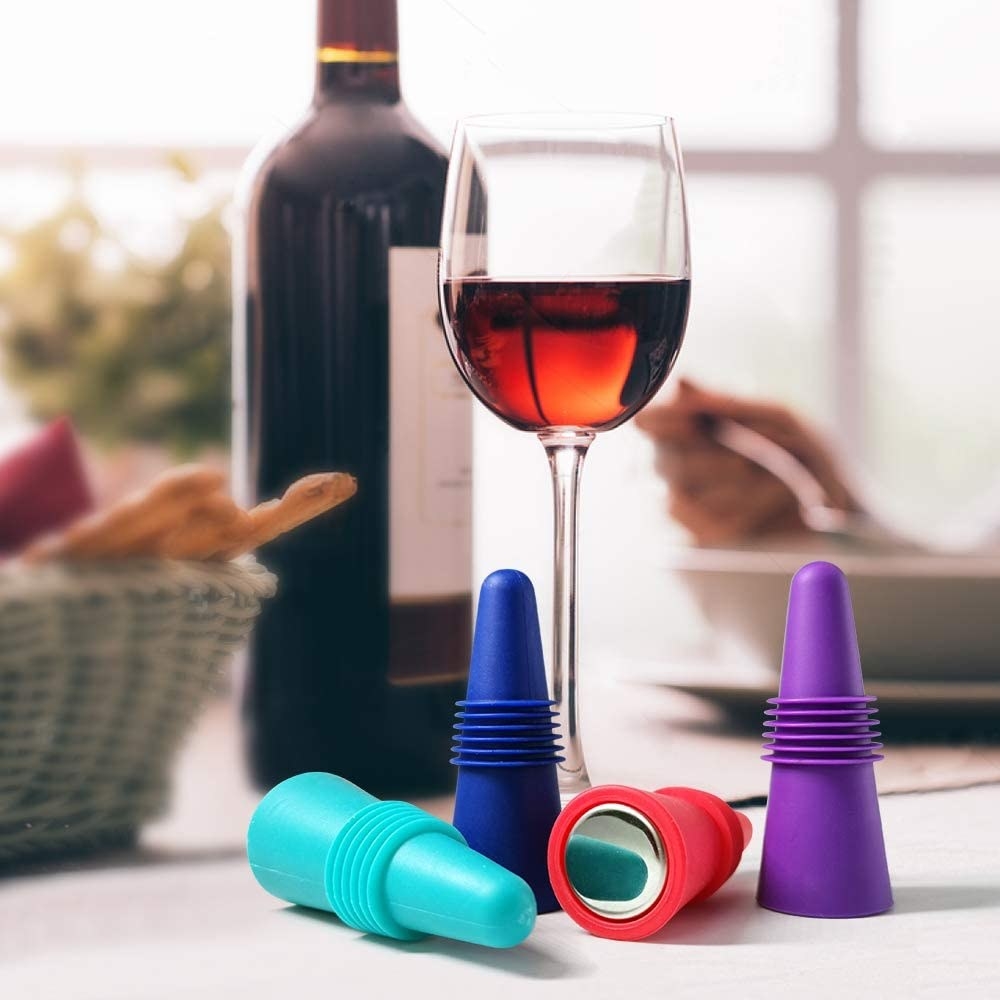 four colored wine stoppers next to a full glass of red wine