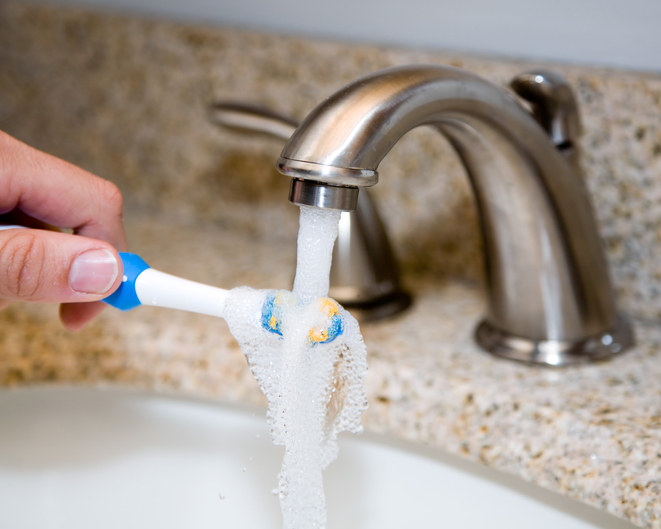 Someone runs their toothbrush under water at the sink