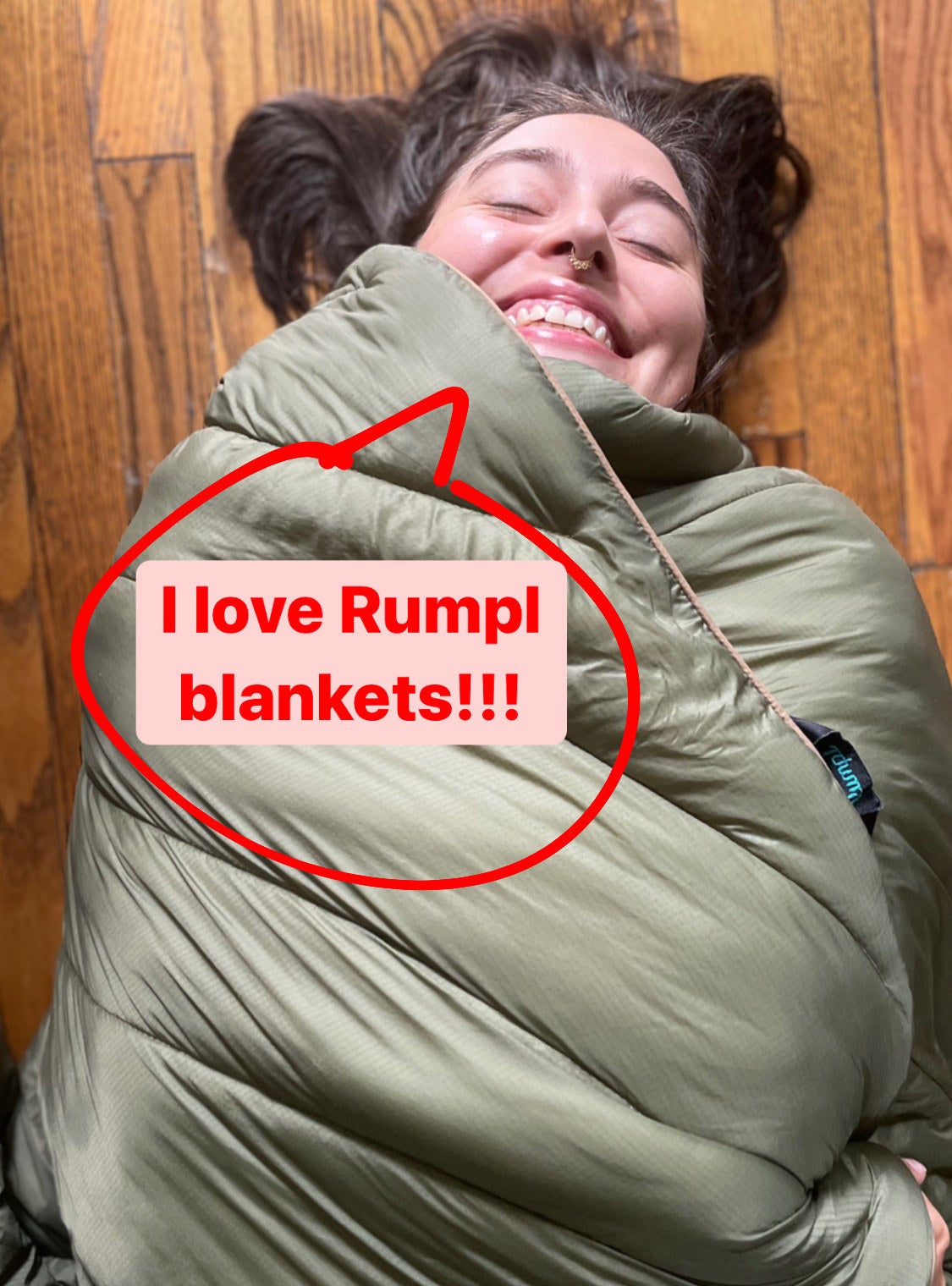 the writer laying on the floor wrapped in the blanket with a speech bubble saying &quot;I love Rumpl blankets&quot;