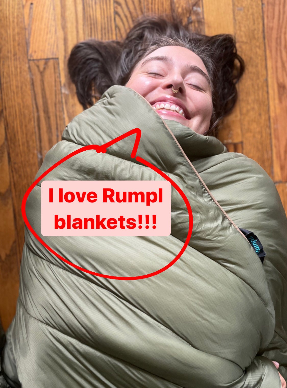 the writer laying on the floor wrapped in the blanket with a speech bubble saying "I love Rumpl blankets"