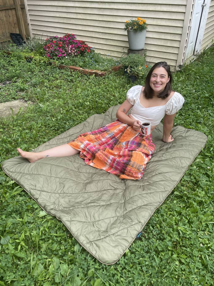 the writer laying sitting with a leg extended on a green puffy blanket