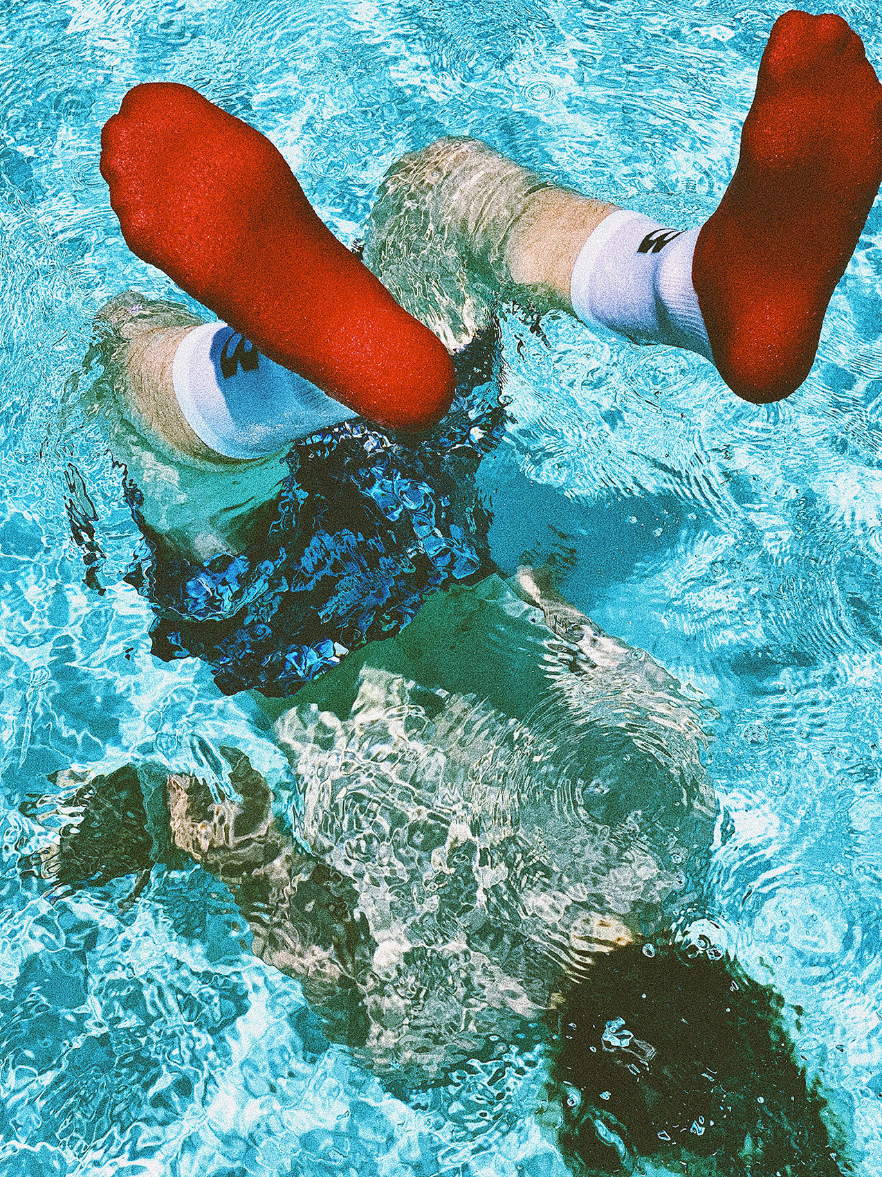 A person diving into a pool with socks on above the water