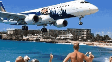 A plane flying low over a beach full of people