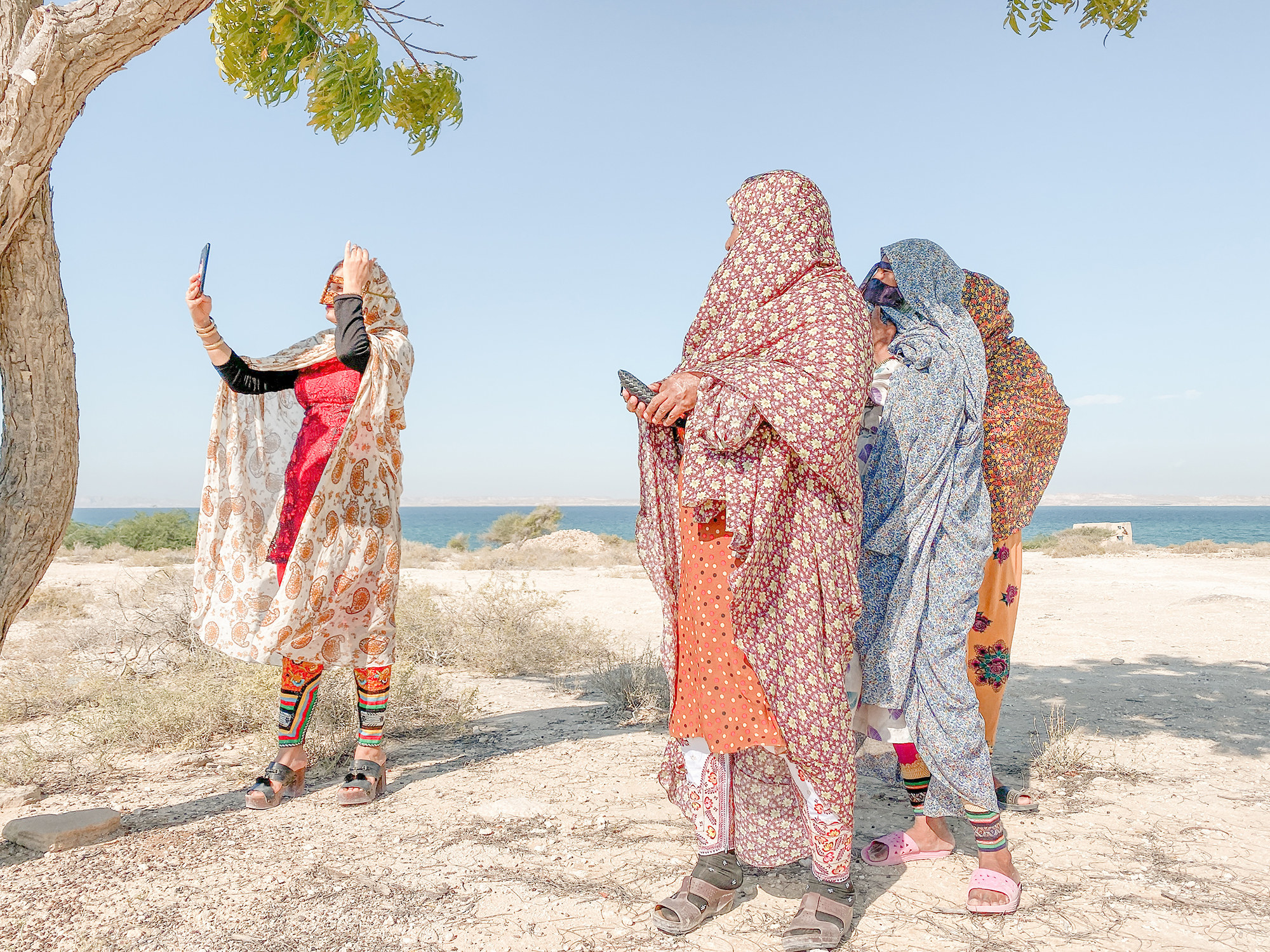 Four women in burkas standing on the seashore holding up their phones and taking selfies