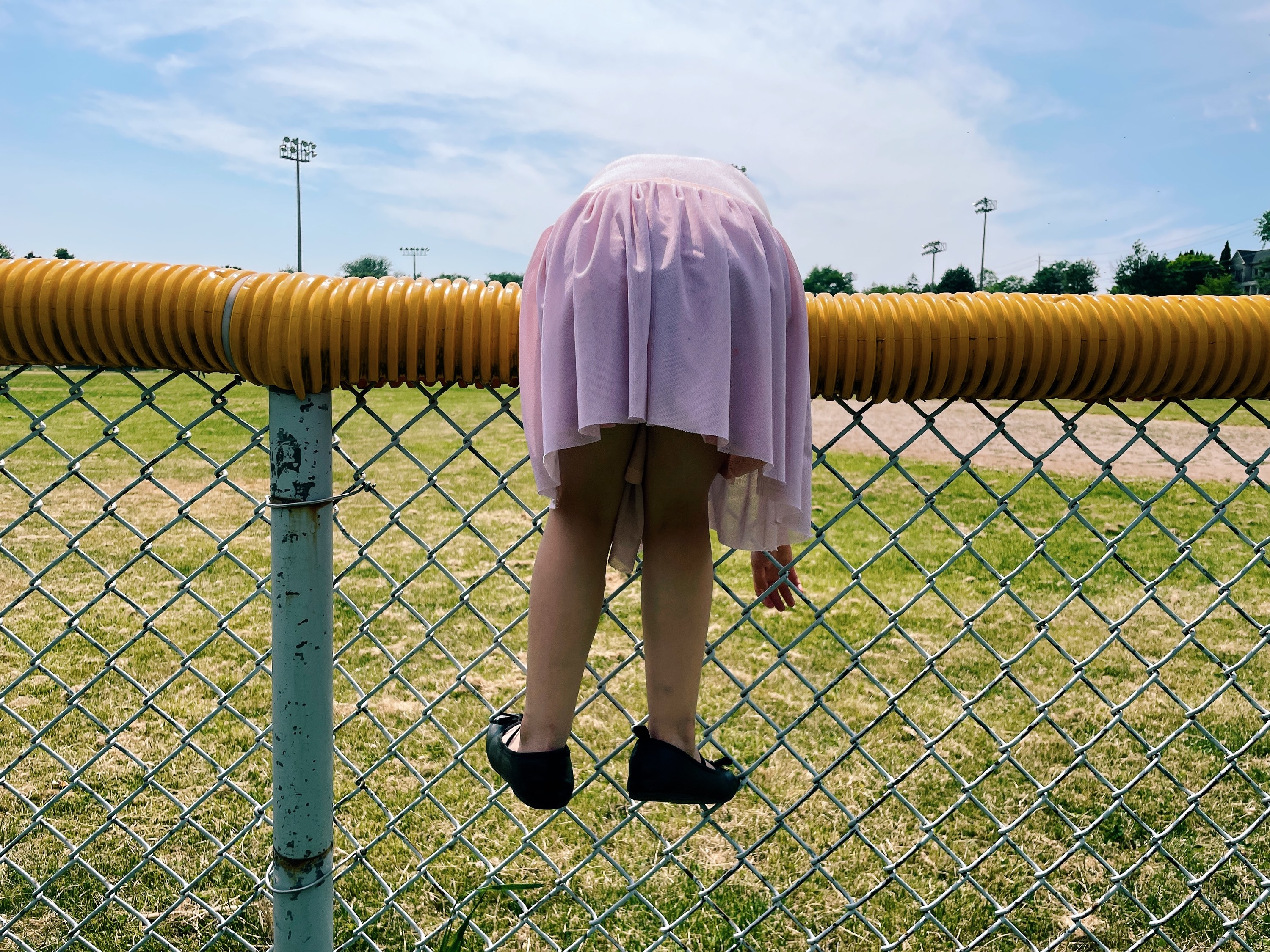 A girl in a dress hangs over a fence