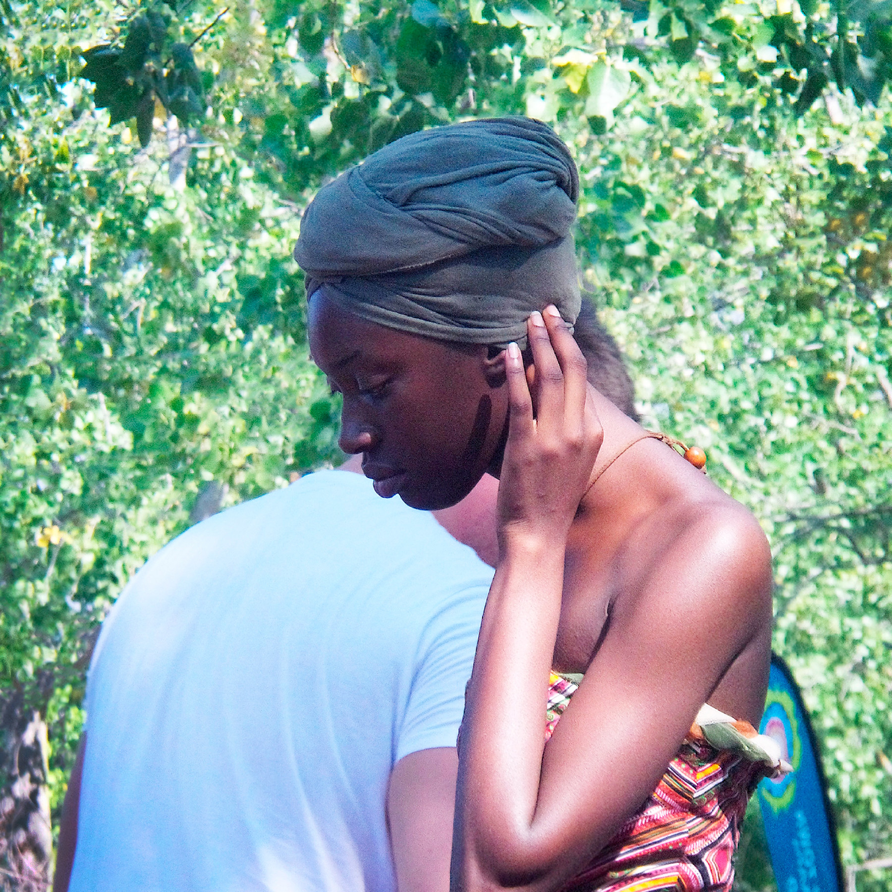 A woman wearing a head wrap and holding a hand to her face crosses paths with a man outside