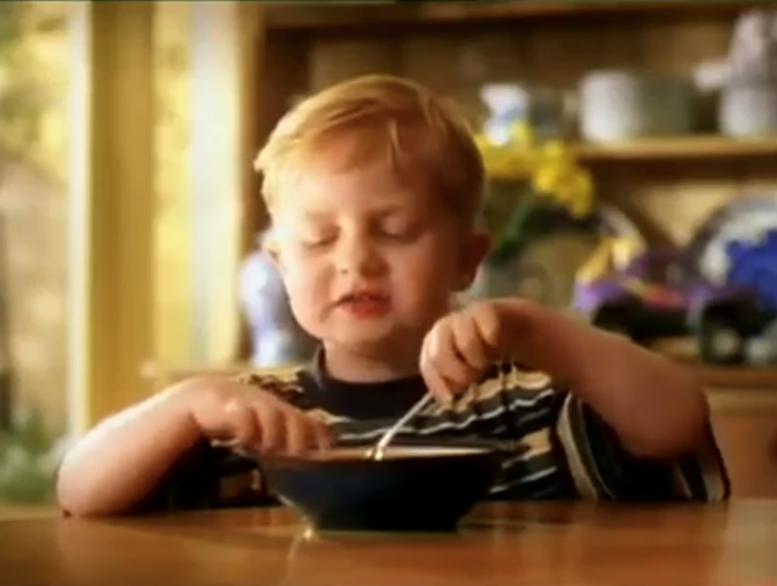 A young boy sits on a table and eats from a bowl filled with SPC fruit