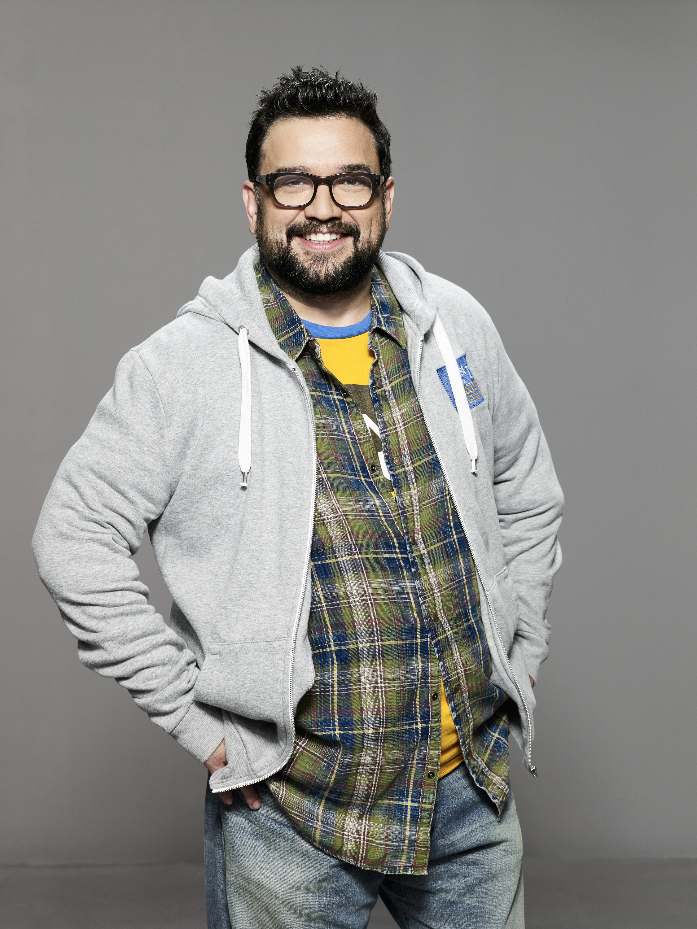 Sanz puts his hands in his pockets while wearing a hoodie, a button-down, and a T-shirt in a promotional image