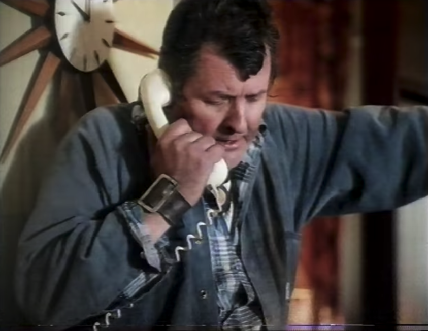 A man talking on the phone; it is a landline phone and he is holding it to his ear