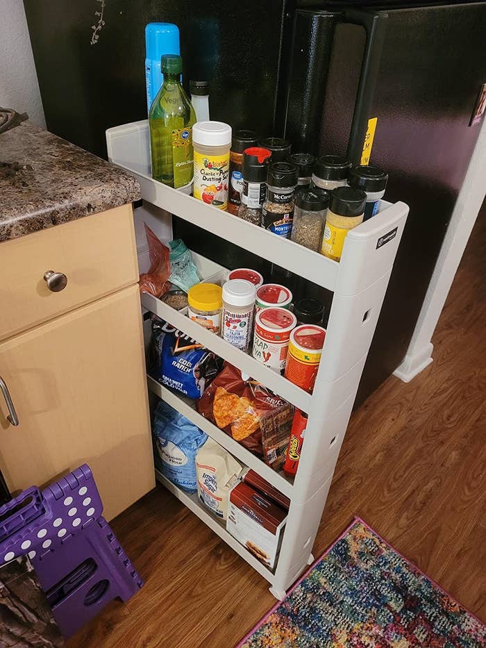 reviewer image of the rolling cart filled with spices wedged between a fridge and a counter