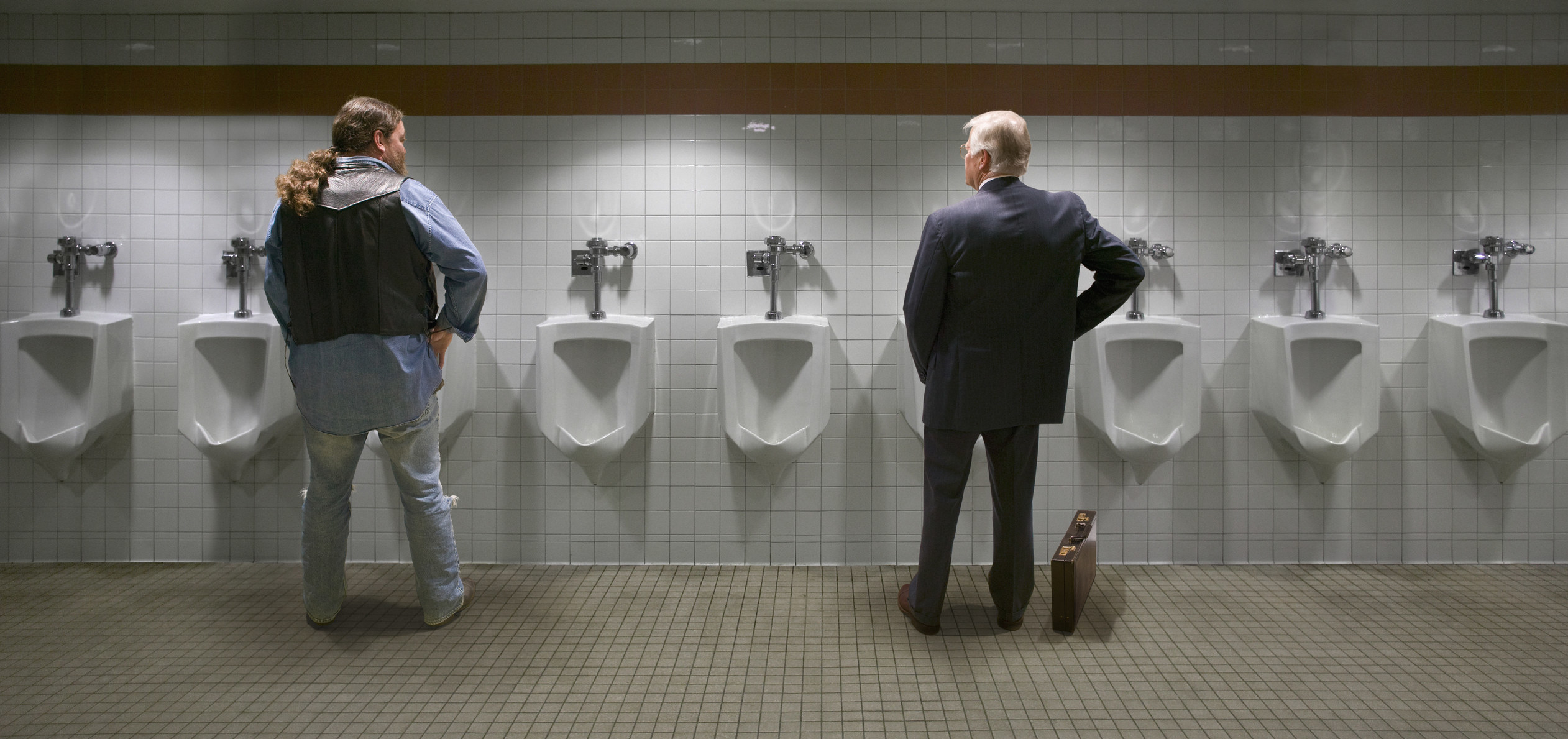Two people standing at urinals with space in between. 