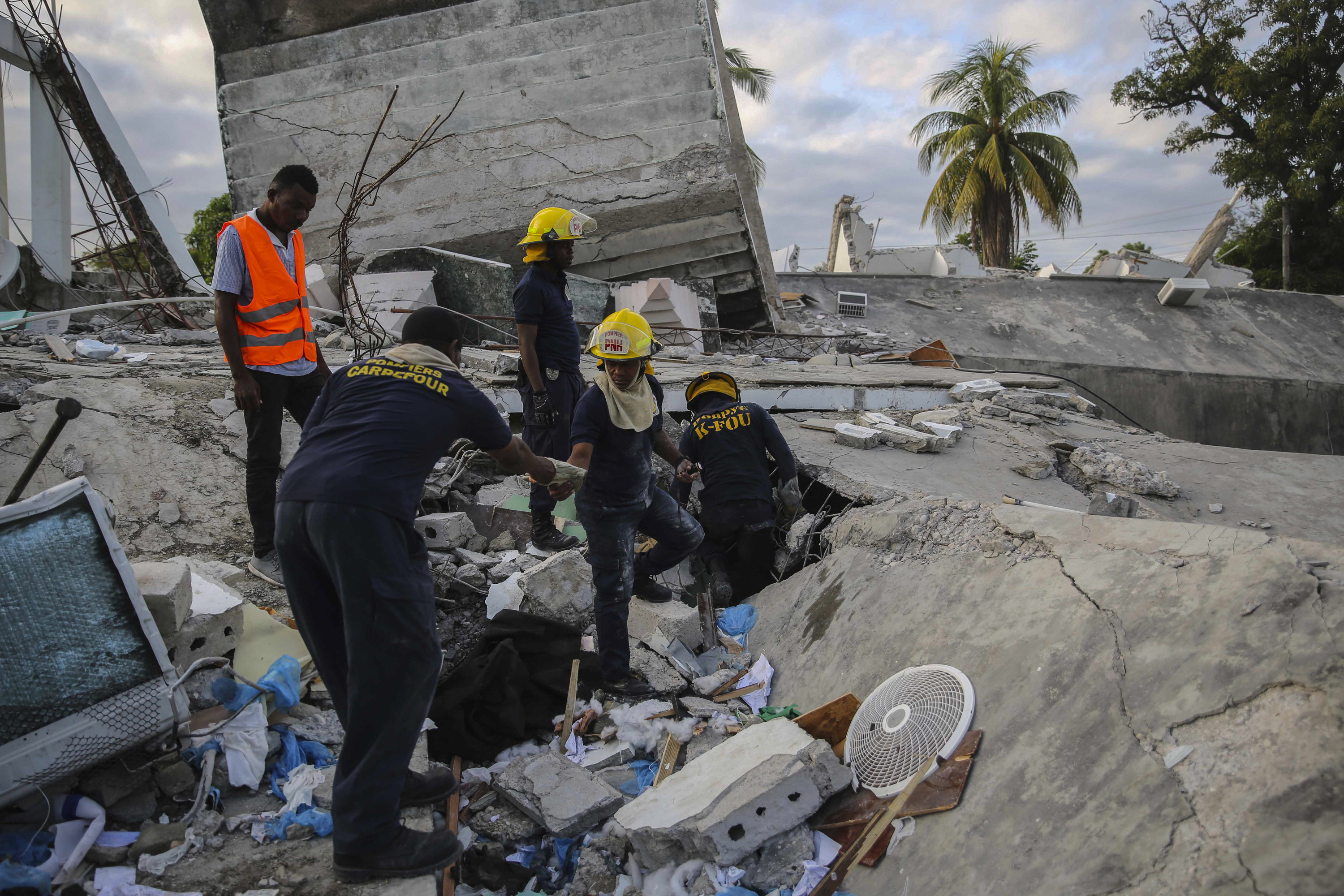 Five people, some in headgear, walk amid the rubble