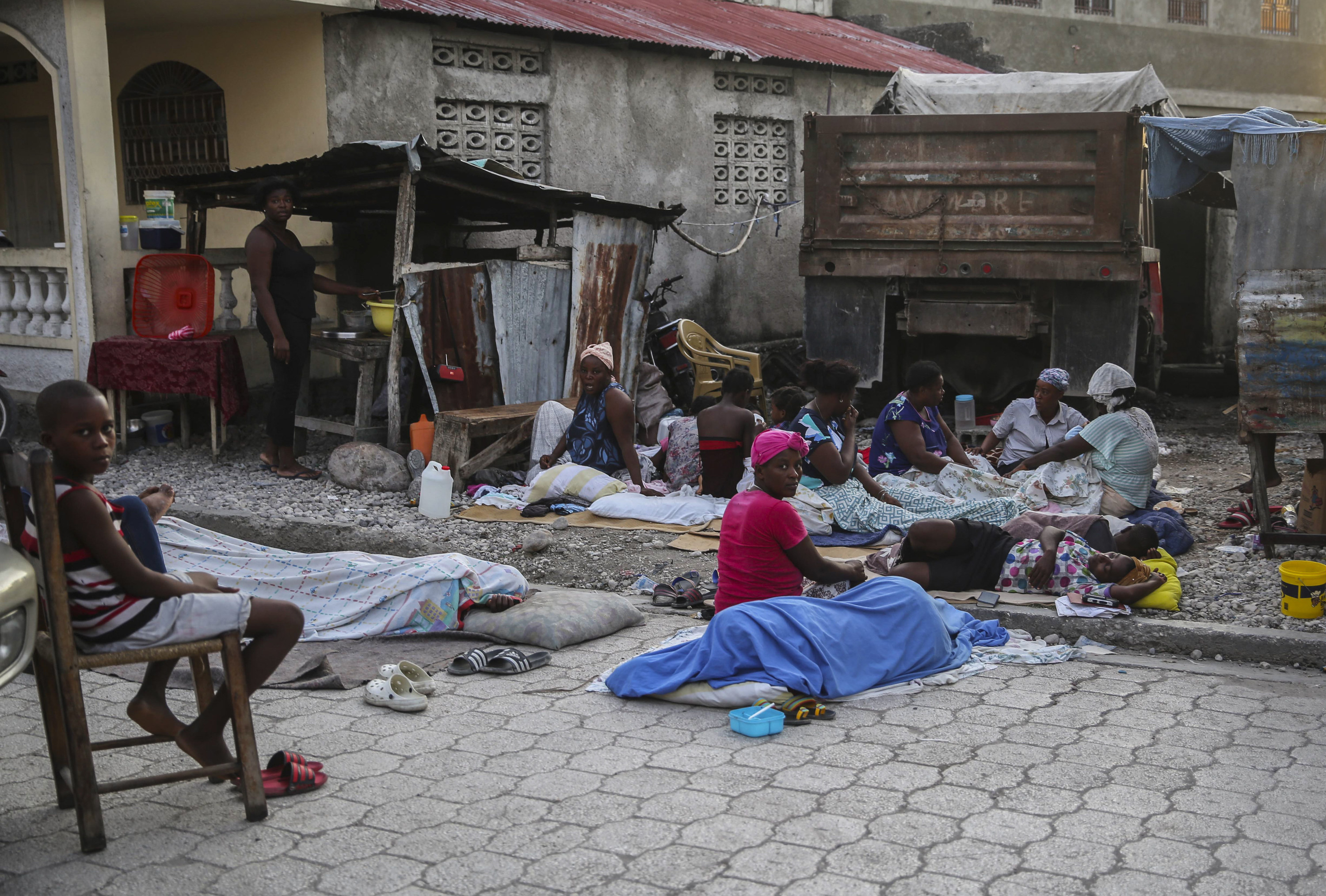 People sit outside and others lie, covered, on the ground