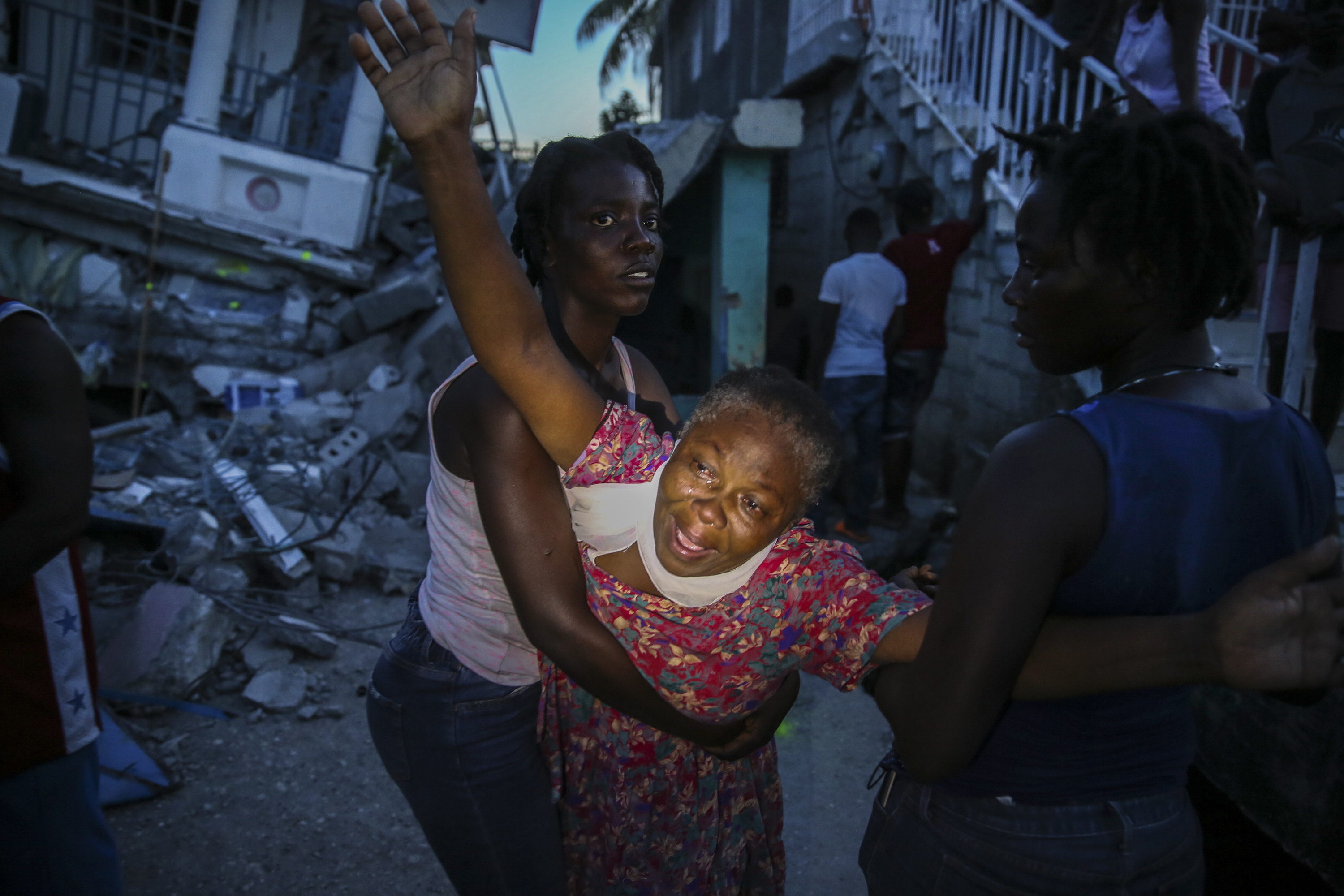 A woman weeps with her arms extended out as she is held by two people 