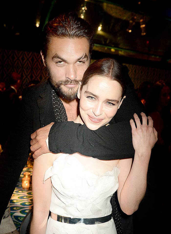 Jason stands behind Emilia with his arm around her neck and her touching his arm