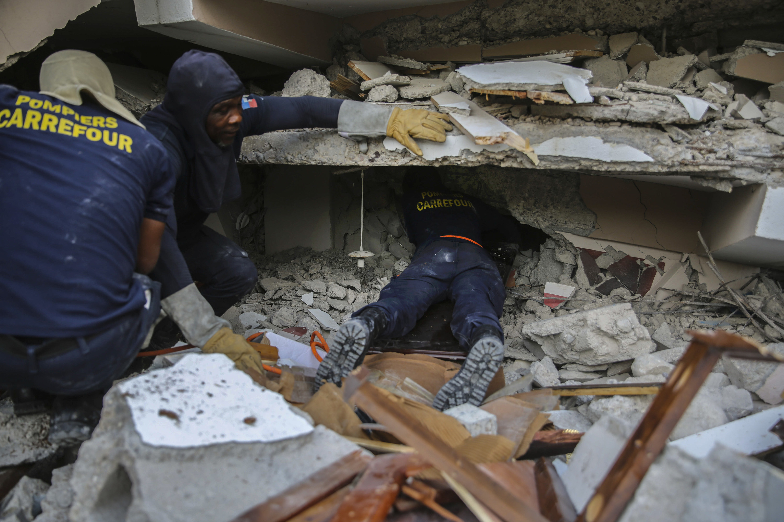 Three people crouch or lie flat amid rubble