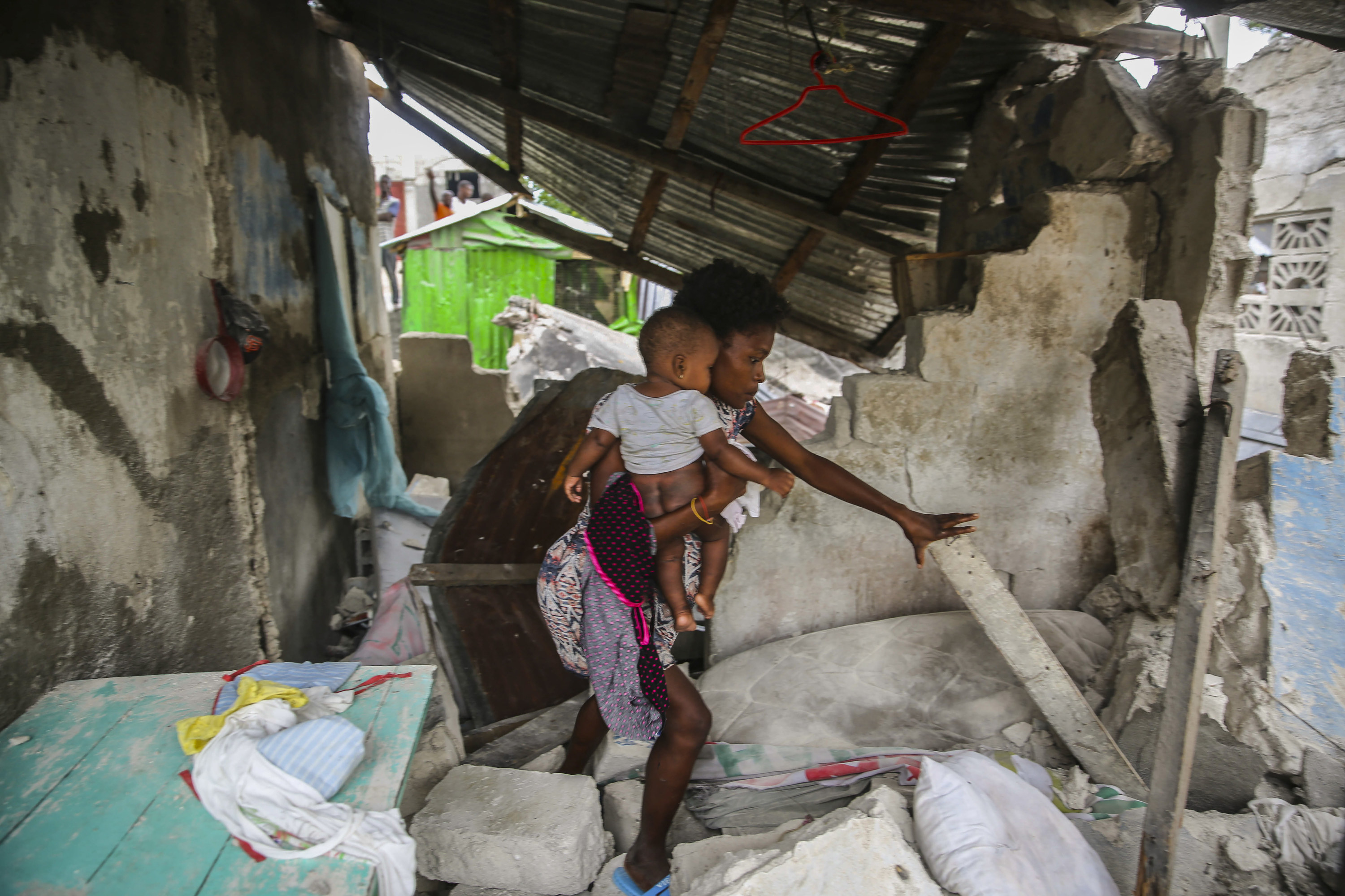 A woman steadies herself against a plank as she holds her baby, who is bare-bottomed