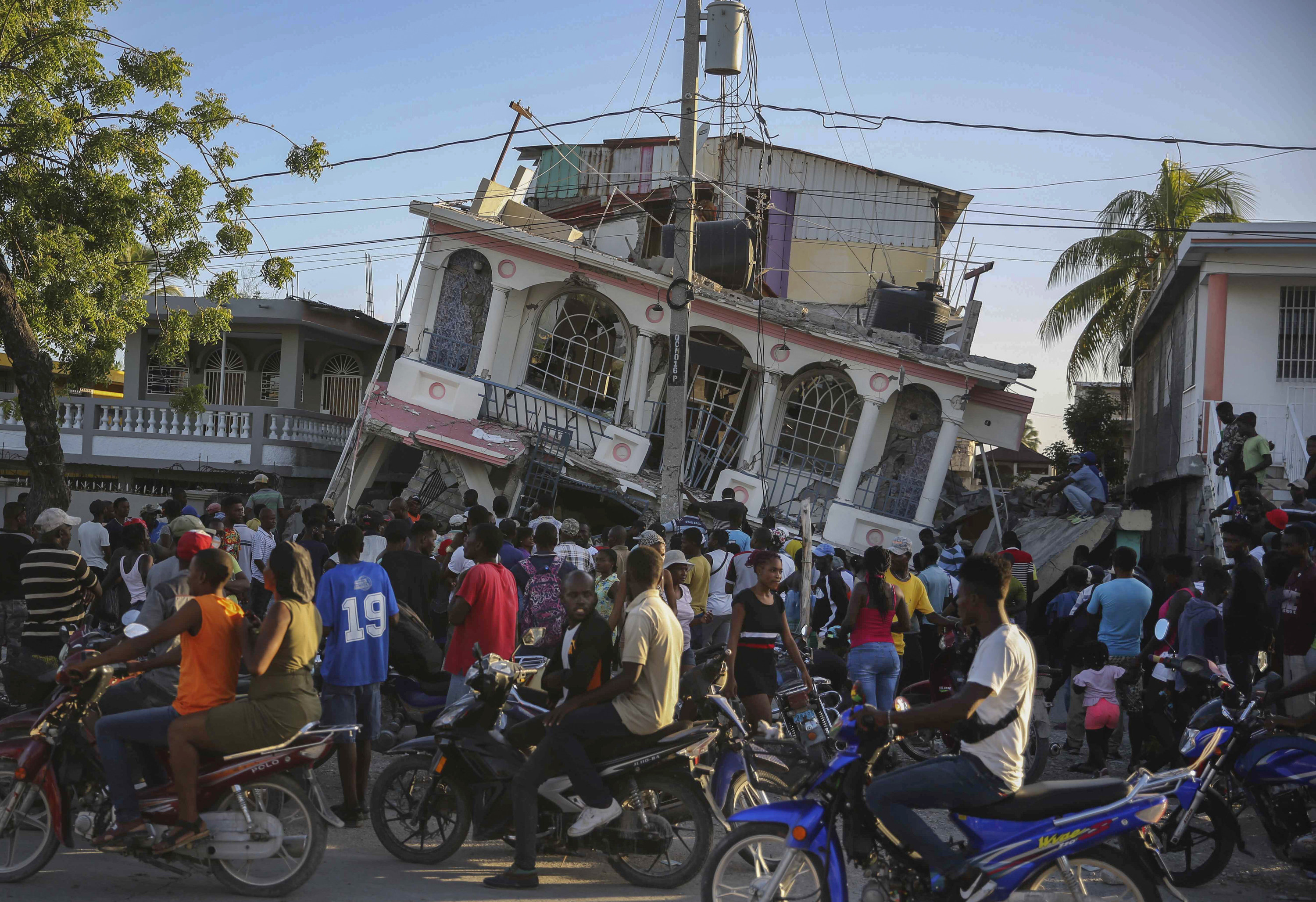 A crowd stands in front of a building sloping down precariously