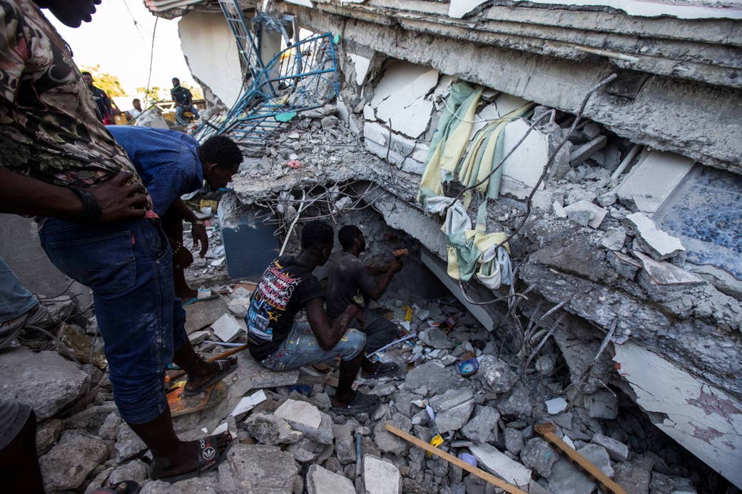 People crouch and sit near extensive rubble