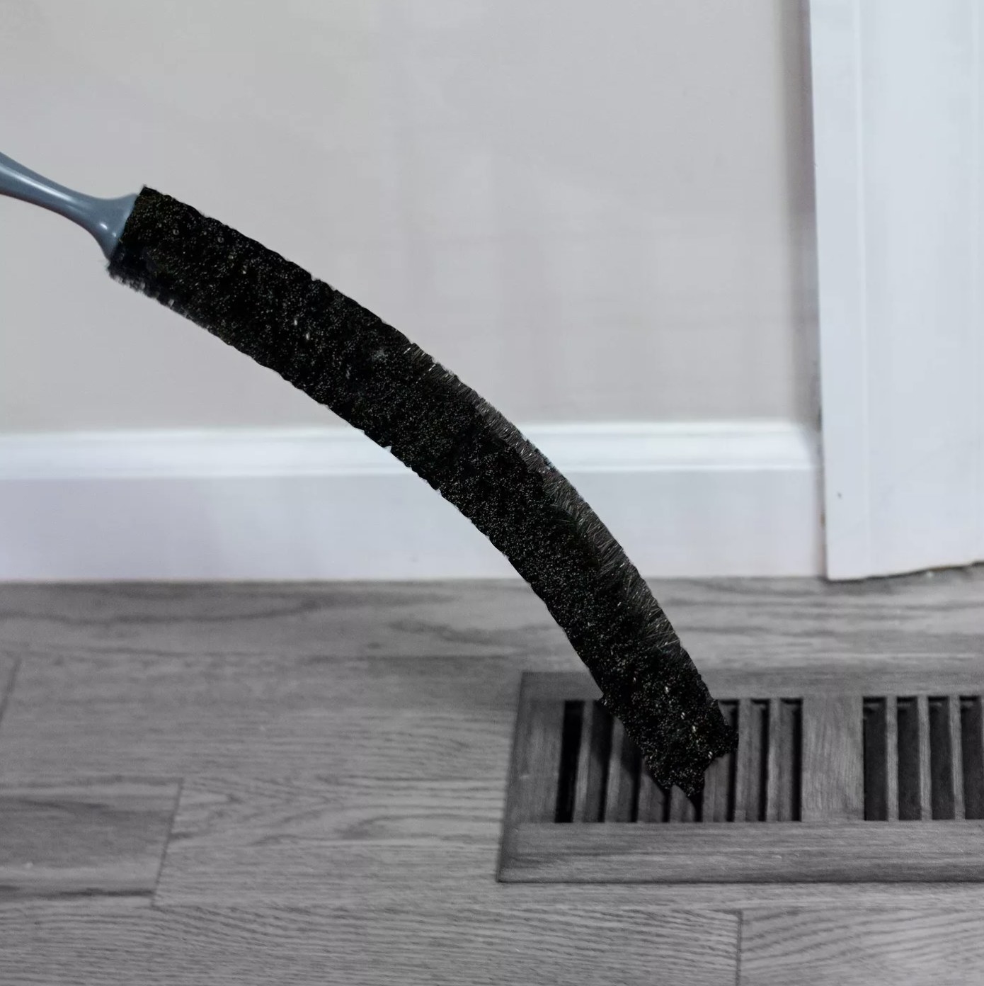 The black brush is angled into a wooden vent on the floor