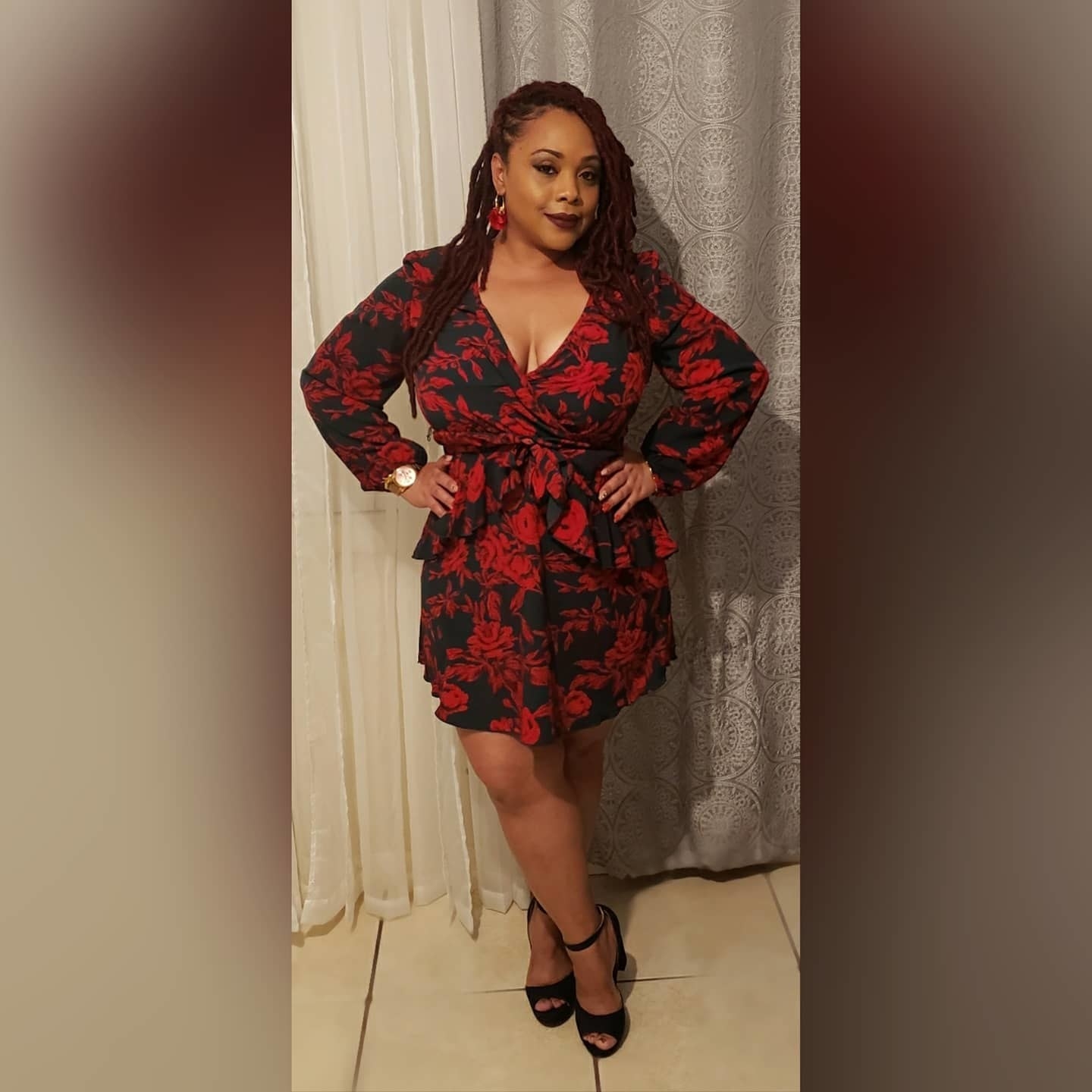 reviewer wearing the black long-sleeve dress, which has a red floral pattern on it, with black ankle strap heels