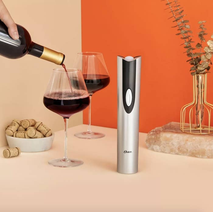 The silver wine opener is in a neutral and warm toned display with red wine and says &quot;Oster&quot; with has black detailing