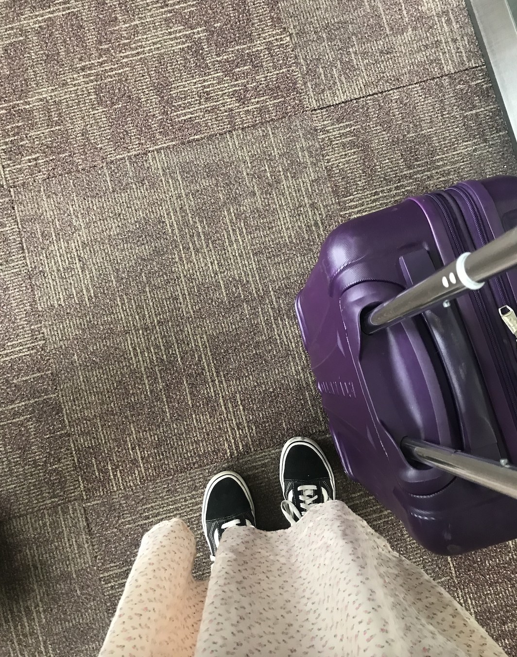 Image of a person&#x27;s feet with a rolly carry-on suitcase