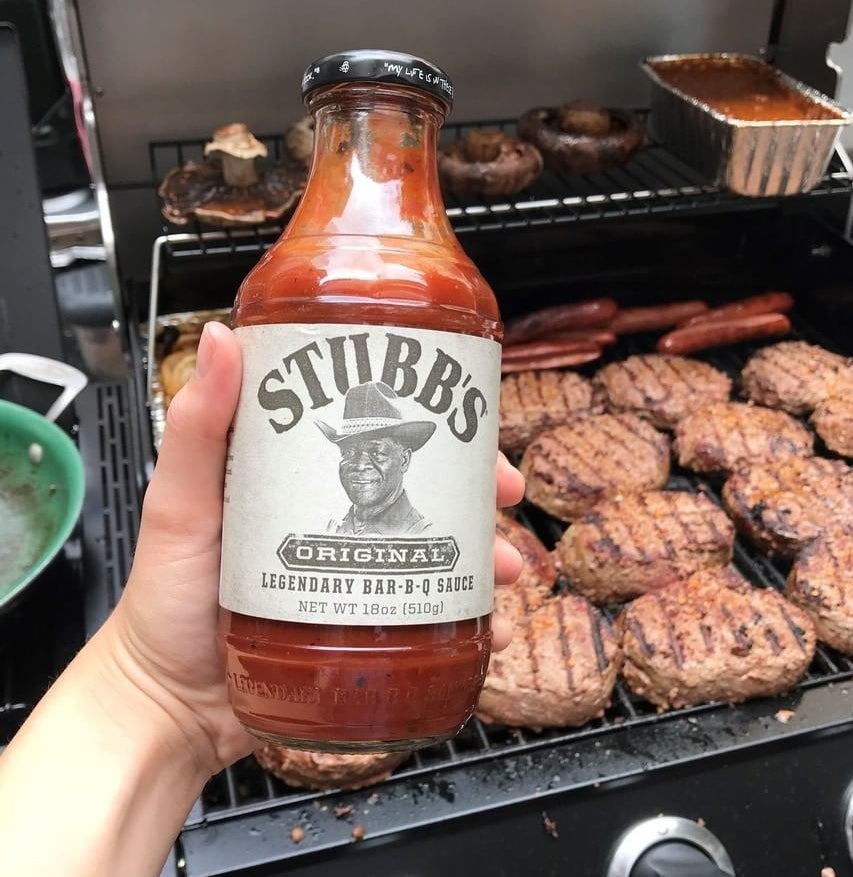 A person holding a bottle of the sauce in front of a grill