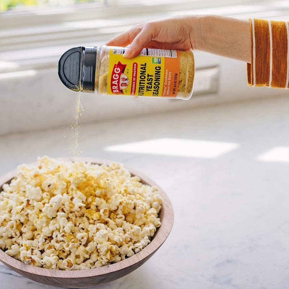 A person shaking the nutritional yeast over popcorn
