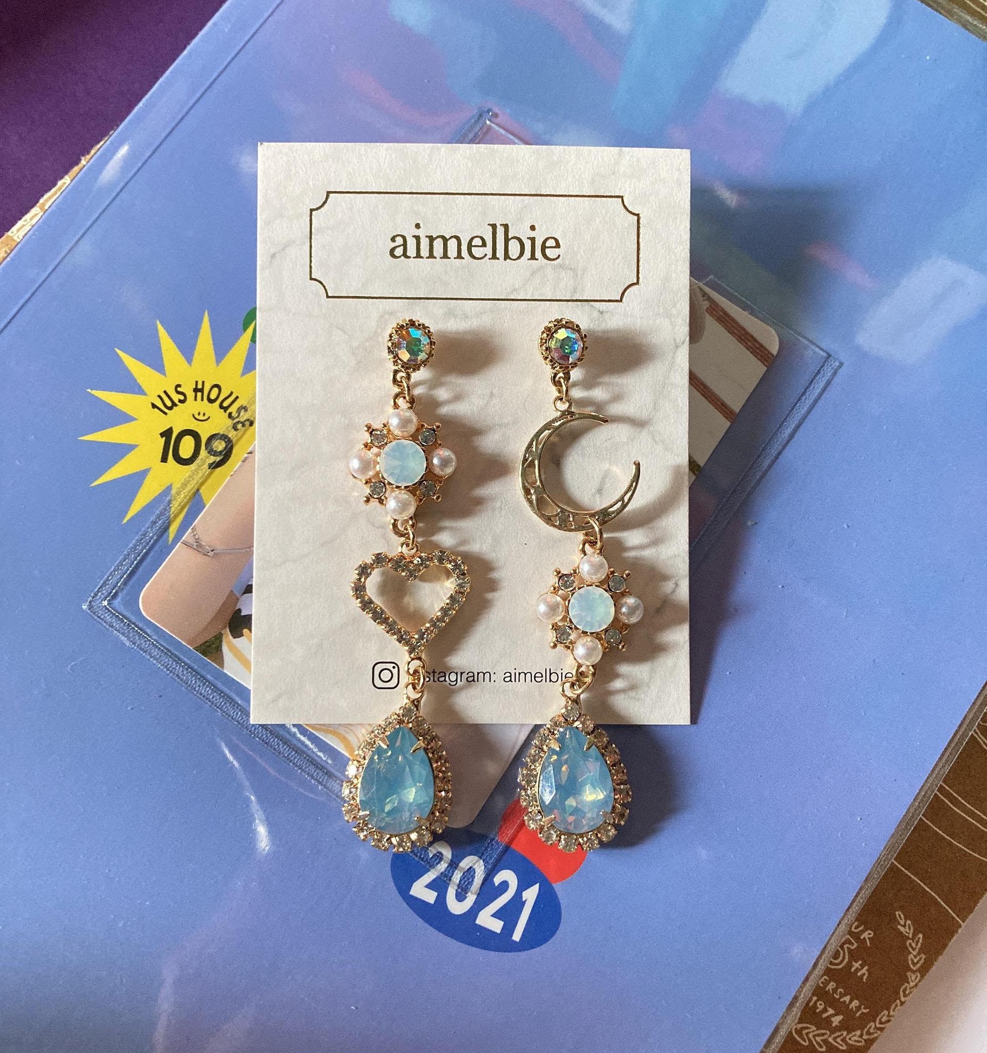 coordinating gold dangly earrings with light blue stones, one with a heart and one with a moon