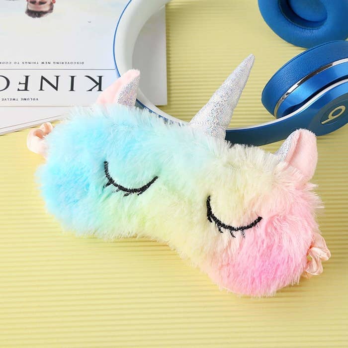 A multicoloured unicorn eye mask with a silver horn and closed eyes embroidered on it