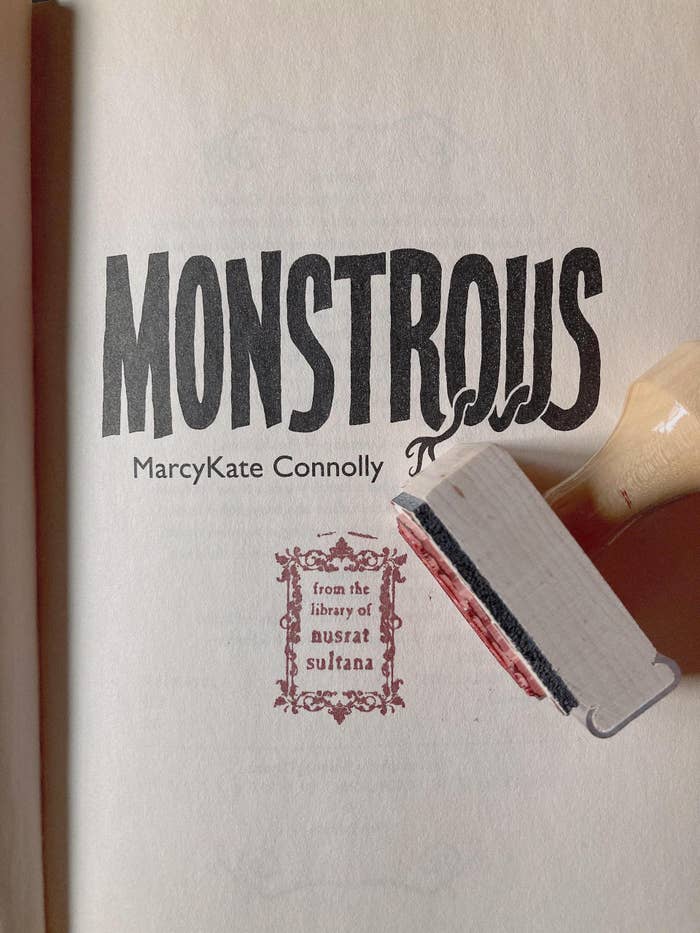 the title page of the book &quot;monstrous&quot; stamped with &quot;from the library of nusrat sultana&quot; on it in red ink, and the stamp with a handle sitting on the page