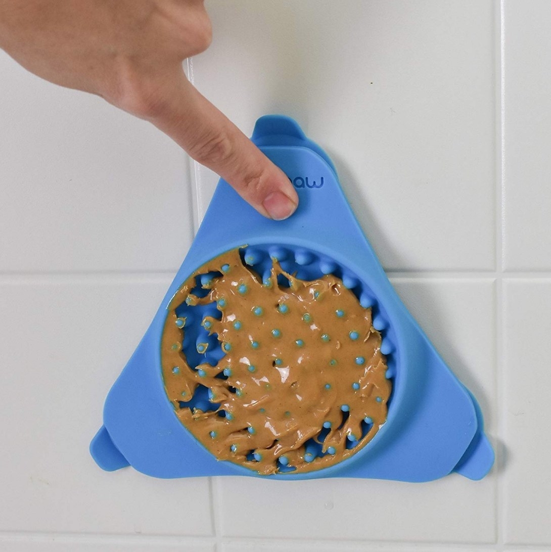 A model pressing a blue, silicone lick mat filled with peanut butter against a shower wall