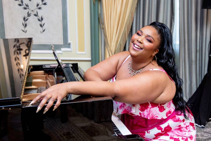 Lizzo smiling and sitting at a piano
