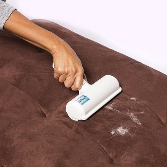 A model using a pet hair remover to remove cat hair from an ottoman
