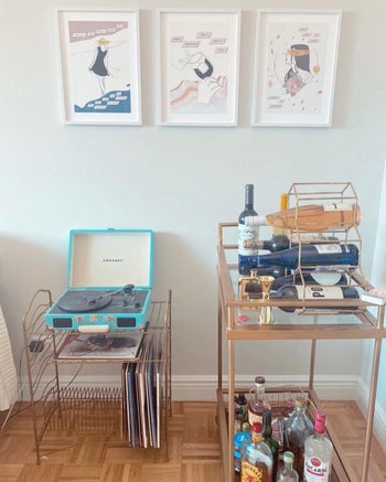 three printables featuring illustrations and lyrics hung on a wall over a bar cart and record player